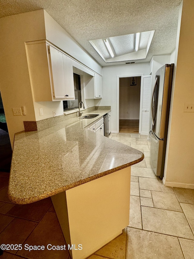 kitchen with appliances with stainless steel finishes, white cabinetry, sink, kitchen peninsula, and light stone countertops