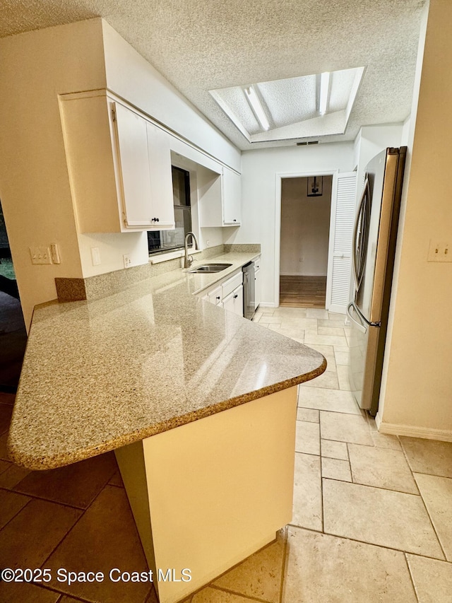 kitchen featuring white cabinetry, appliances with stainless steel finishes, kitchen peninsula, and light stone counters