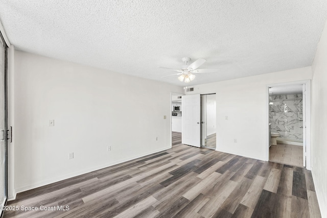 unfurnished bedroom with dark wood-type flooring, ceiling fan, connected bathroom, and a textured ceiling