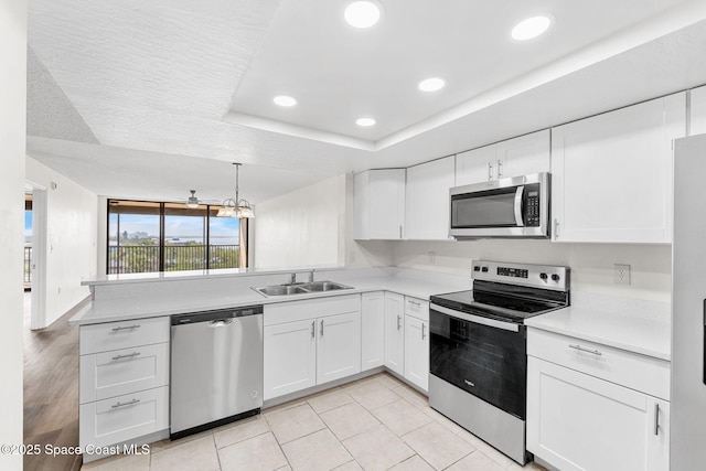 kitchen featuring sink, appliances with stainless steel finishes, white cabinets, decorative light fixtures, and a raised ceiling