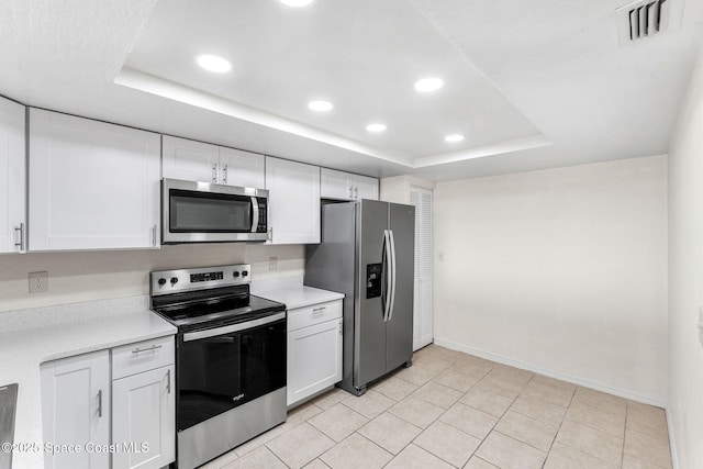 kitchen with light tile patterned floors, a tray ceiling, stainless steel appliances, and white cabinets