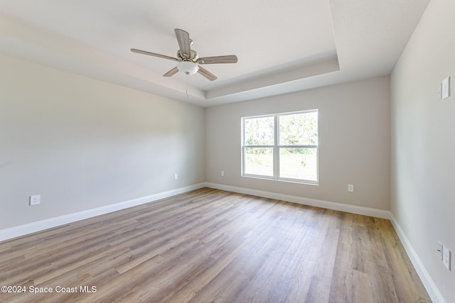 unfurnished room with a tray ceiling, ceiling fan, and light wood-type flooring