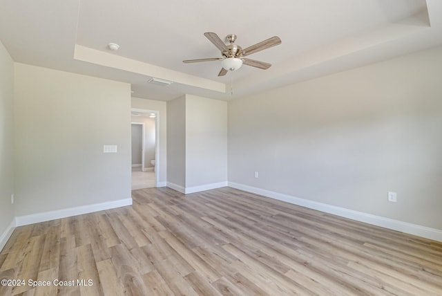 empty room featuring ceiling fan, a raised ceiling, and light wood-type flooring