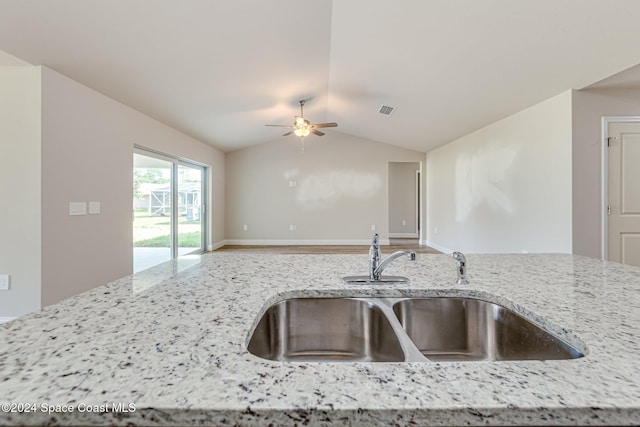 kitchen featuring ceiling fan, light stone countertops, lofted ceiling, and sink