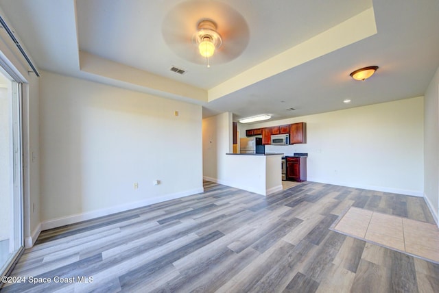 unfurnished living room featuring hardwood / wood-style flooring, ceiling fan, and a raised ceiling