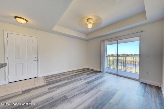 spare room featuring ceiling fan, a tray ceiling, and light hardwood / wood-style flooring