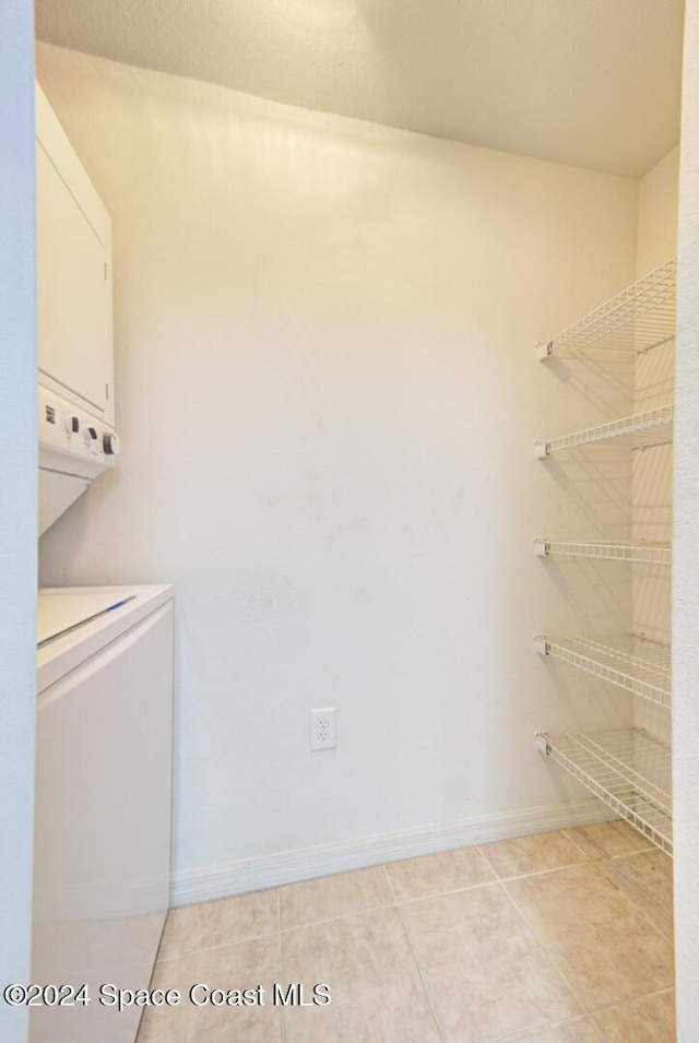 laundry area with light tile patterned floors and stacked washing maching and dryer