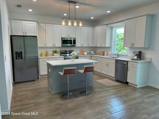 kitchen with white cabinetry, sink, decorative light fixtures, a kitchen island, and appliances with stainless steel finishes