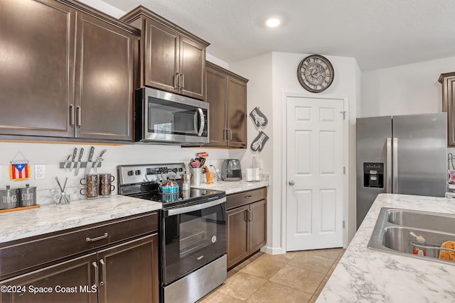 kitchen with appliances with stainless steel finishes, dark brown cabinetry, a textured ceiling, sink, and light tile patterned floors