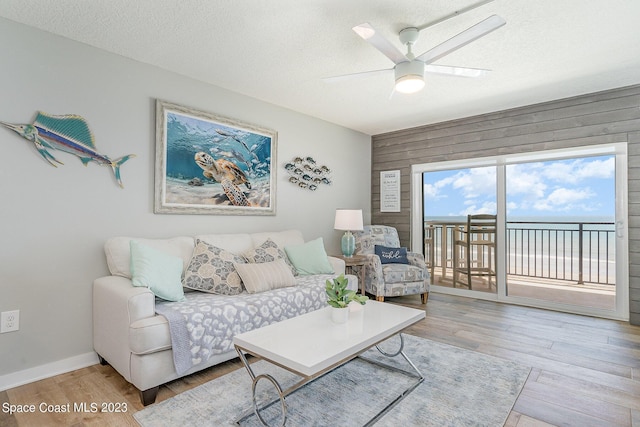 living room featuring ceiling fan, wood walls, a water view, and light wood-type flooring