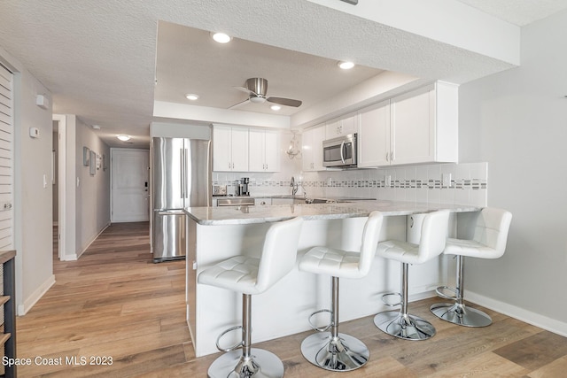 kitchen featuring kitchen peninsula, appliances with stainless steel finishes, decorative backsplash, a kitchen breakfast bar, and white cabinetry