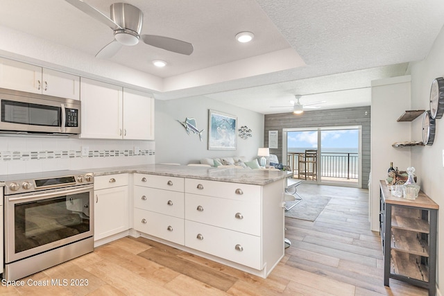 kitchen with backsplash, kitchen peninsula, light wood-type flooring, appliances with stainless steel finishes, and white cabinetry