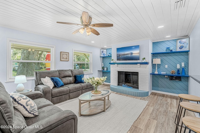 living room with wooden walls, a brick fireplace, ceiling fan, light hardwood / wood-style floors, and wood ceiling