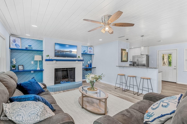 living room featuring ceiling fan, light hardwood / wood-style flooring, wooden walls, a fireplace, and wood ceiling