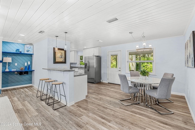 kitchen featuring kitchen peninsula, stainless steel fridge, pendant lighting, white cabinets, and light hardwood / wood-style floors