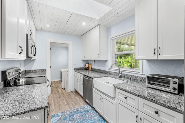 kitchen with sink, appliances with stainless steel finishes, stone countertops, white cabinetry, and washing machine and clothes dryer