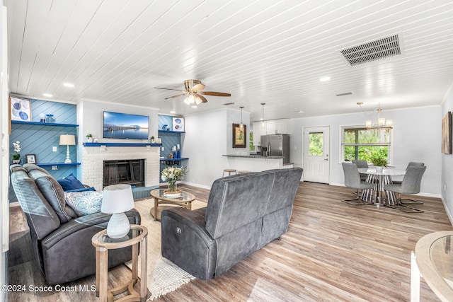 living room featuring ceiling fan, wooden ceiling, a brick fireplace, wooden walls, and light wood-type flooring