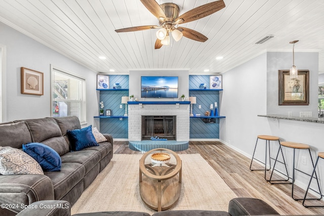 living room featuring ceiling fan, light wood-type flooring, a fireplace, wood ceiling, and ornamental molding