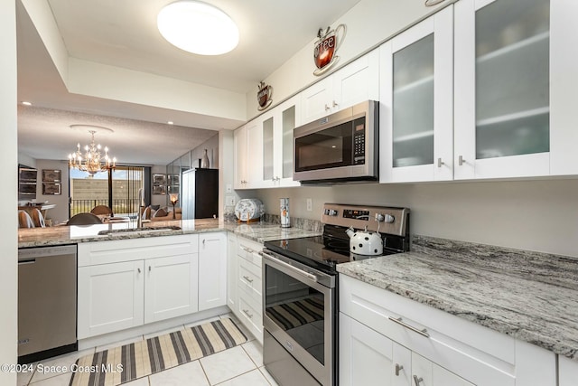 kitchen with stainless steel appliances, sink, light tile patterned floors, an inviting chandelier, and white cabinets