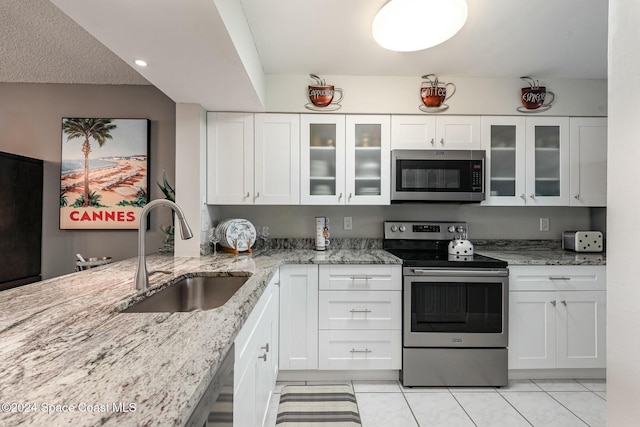 kitchen featuring appliances with stainless steel finishes, light stone counters, sink, white cabinetry, and light tile patterned flooring