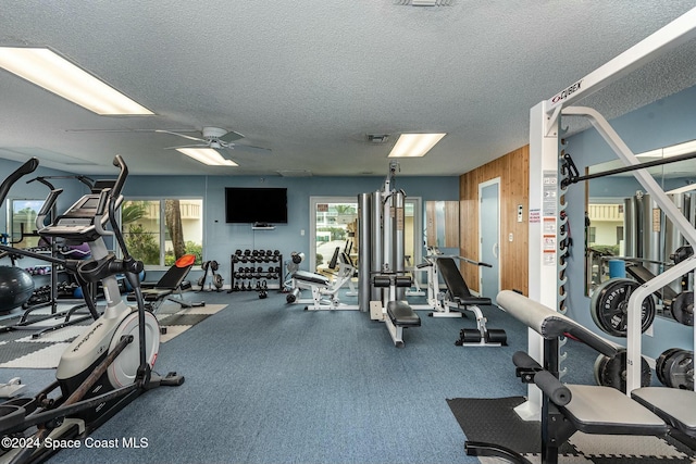 exercise room featuring ceiling fan, plenty of natural light, a textured ceiling, and wooden walls