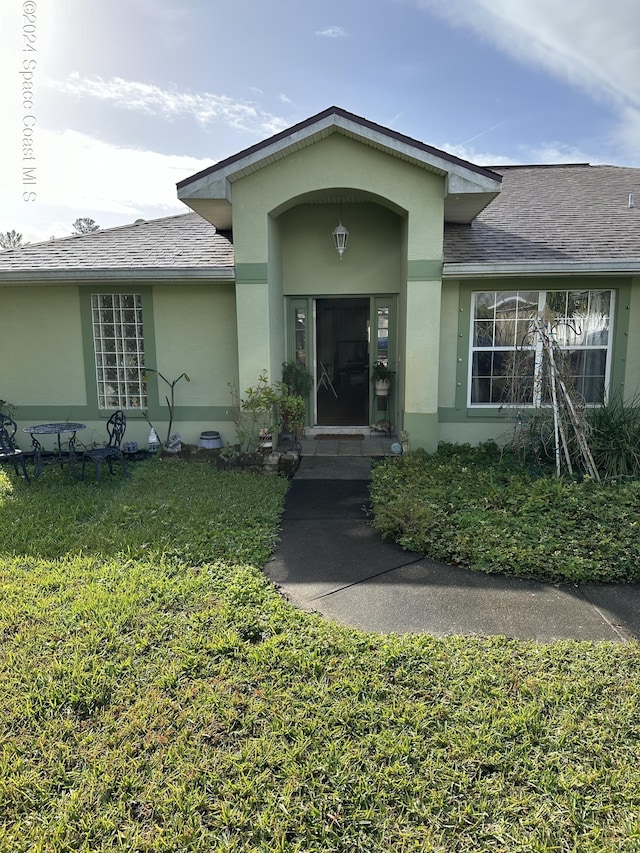 property entrance featuring a yard, roof with shingles, and stucco siding