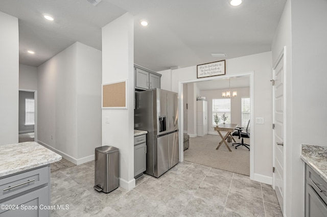 kitchen featuring stainless steel fridge, light stone counters, gray cabinetry, and a notable chandelier