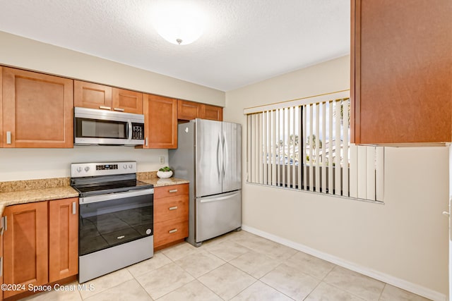 kitchen featuring a textured ceiling, light stone countertops, light tile patterned floors, and stainless steel appliances