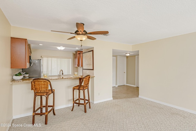 kitchen featuring stainless steel refrigerator, kitchen peninsula, light carpet, and a kitchen bar