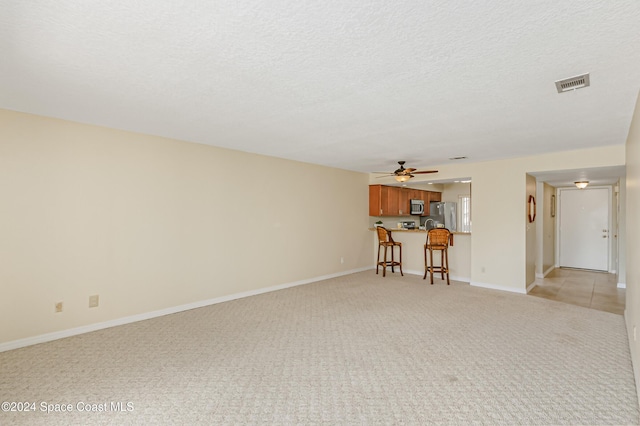 unfurnished living room with a textured ceiling, light colored carpet, and ceiling fan