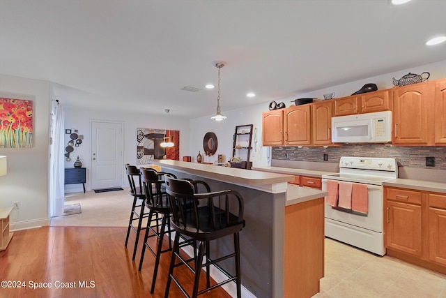 kitchen with a center island, hanging light fixtures, white appliances, a breakfast bar area, and light wood-type flooring