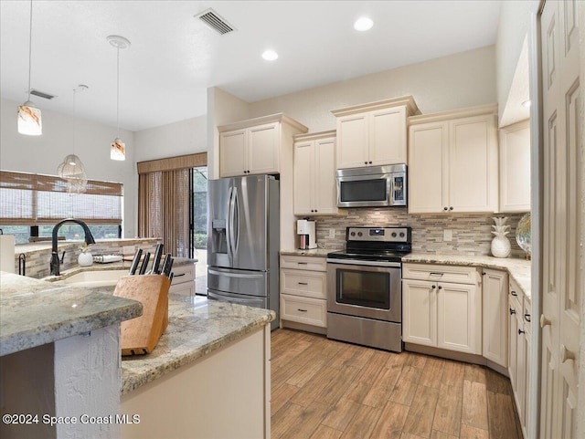 kitchen with light stone countertops, light wood-type flooring, stainless steel appliances, cream cabinetry, and hanging light fixtures