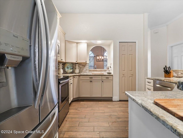 kitchen featuring decorative backsplash, stainless steel appliances, crown molding, a notable chandelier, and light hardwood / wood-style floors