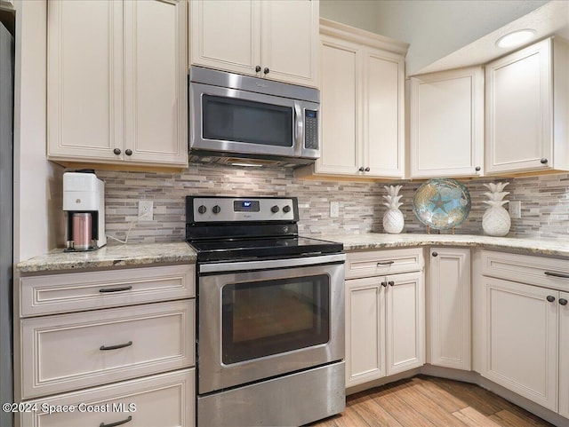 kitchen featuring light stone counters, light hardwood / wood-style flooring, cream cabinets, decorative backsplash, and appliances with stainless steel finishes