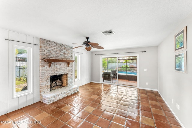 unfurnished living room with tile patterned floors, ceiling fan, a textured ceiling, and a brick fireplace