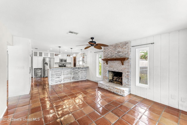 unfurnished living room with ceiling fan, a healthy amount of sunlight, dark tile patterned floors, and a fireplace