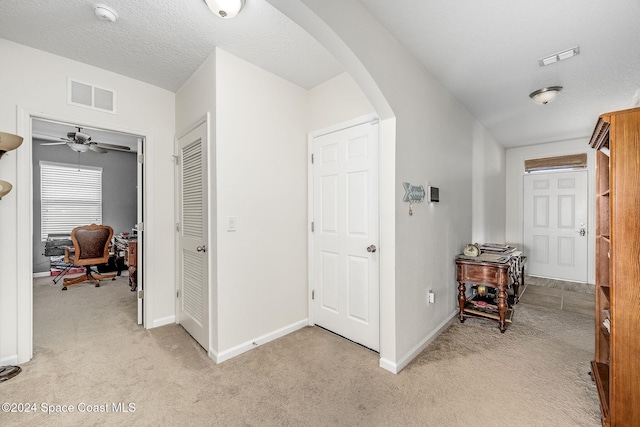 hallway with light colored carpet and a textured ceiling