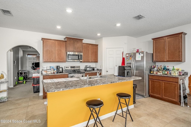 kitchen with a kitchen breakfast bar, a textured ceiling, stainless steel appliances, a kitchen island with sink, and sink