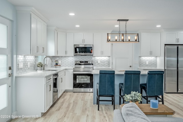 kitchen with sink, stainless steel appliances, light hardwood / wood-style floors, pendant lighting, and white cabinets