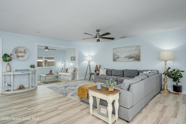 living room featuring ceiling fan, light hardwood / wood-style floors, and a textured ceiling