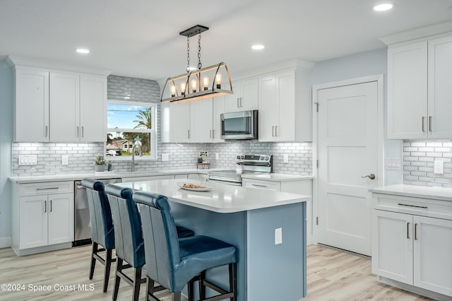 kitchen with stainless steel appliances, white cabinetry, a kitchen island, and light hardwood / wood-style floors