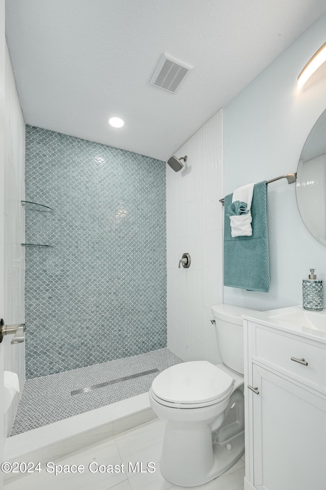 bathroom featuring a tile shower, vanity, toilet, and tile patterned floors