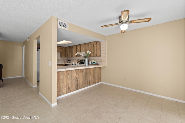 kitchen with decorative backsplash, stainless steel fridge, a textured ceiling, light tile patterned floors, and tile counters