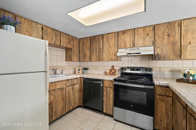 kitchen featuring appliances with stainless steel finishes, backsplash, sink, light tile patterned floors, and tile counters