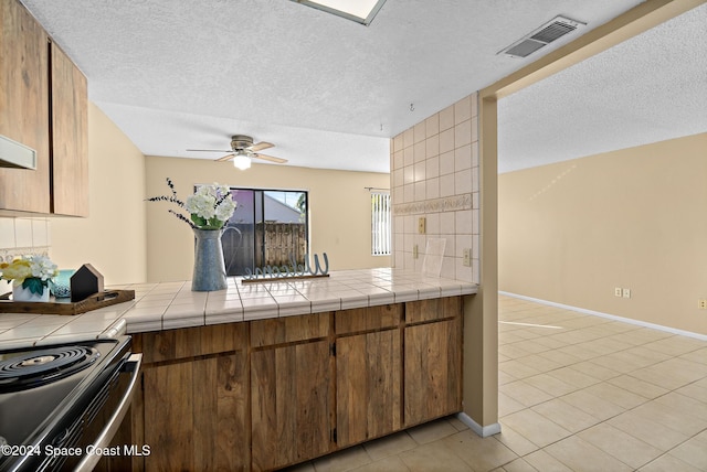 kitchen with electric range, tile counters, light tile patterned flooring, and a textured ceiling