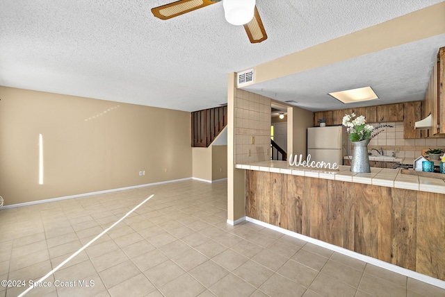 kitchen with a textured ceiling, tile counters, white fridge, and backsplash