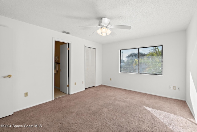 unfurnished bedroom featuring light carpet, a textured ceiling, ensuite bath, and ceiling fan