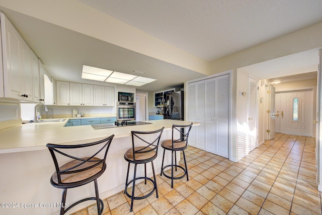 kitchen with kitchen peninsula, a breakfast bar, white cabinets, and black appliances