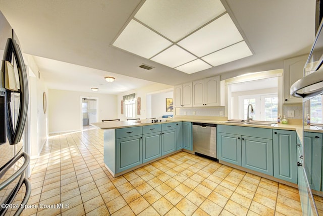 kitchen with kitchen peninsula, decorative backsplash, stainless steel appliances, sink, and white cabinets