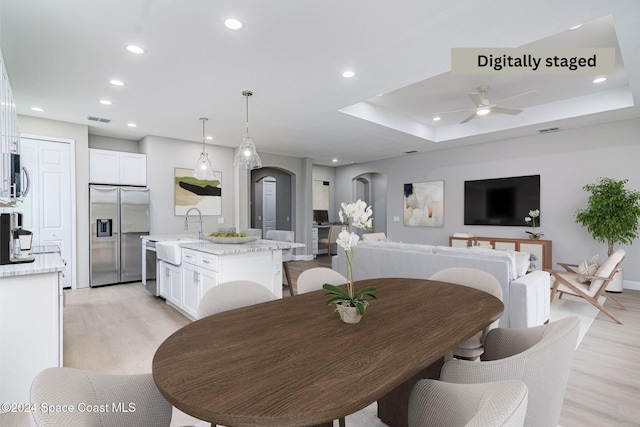 dining space with ceiling fan, light wood-type flooring, sink, and a tray ceiling